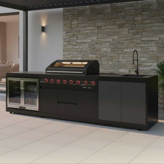 Outdoor kitchen with black grill and refrigerator against a stone wall.